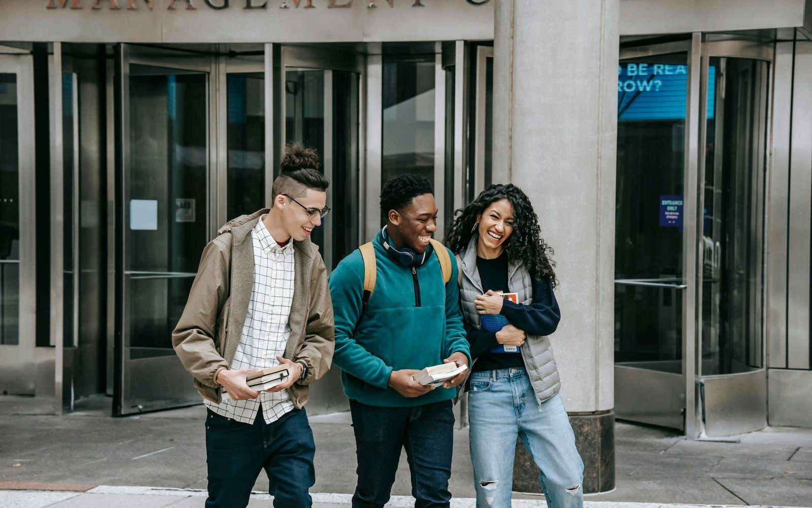 Young cheerful multiethnic students with books having fun on urban pavement while speaking in daylight